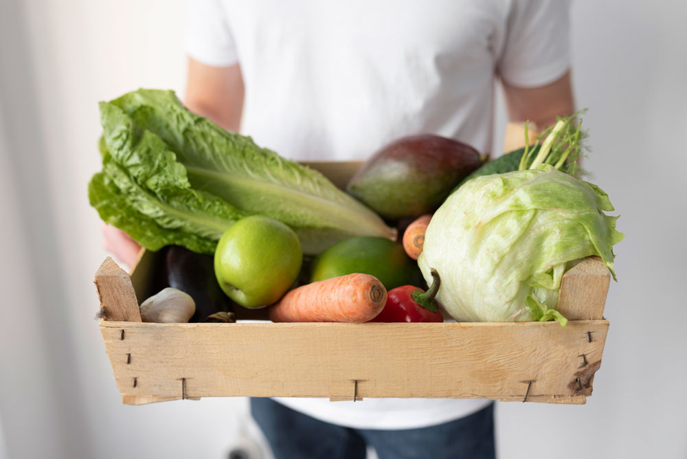 Persona agarrando una caja de madera llena de frutas y verduras